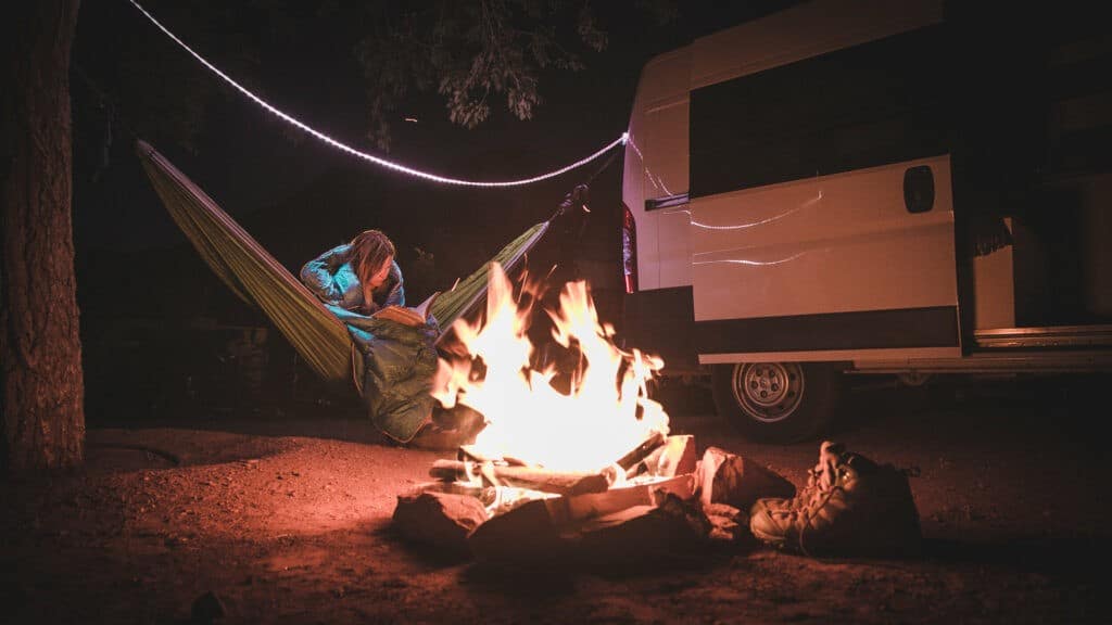 Reading in a hammock by a fire and campervan