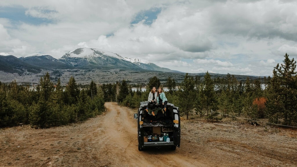 2 people sitting on the top of a campervan with a mountain behind
