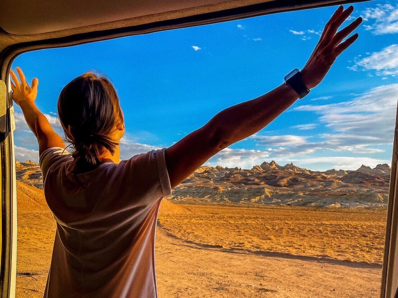 A person stretching and taking in the view from a Campervan
