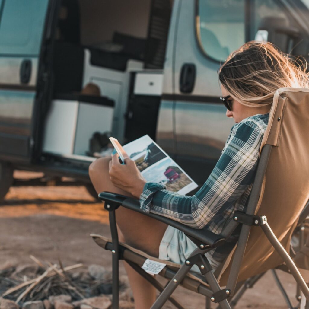 Person reading in a camp chair by a van