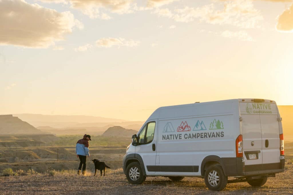 Person with their dog and campervan at sunset
