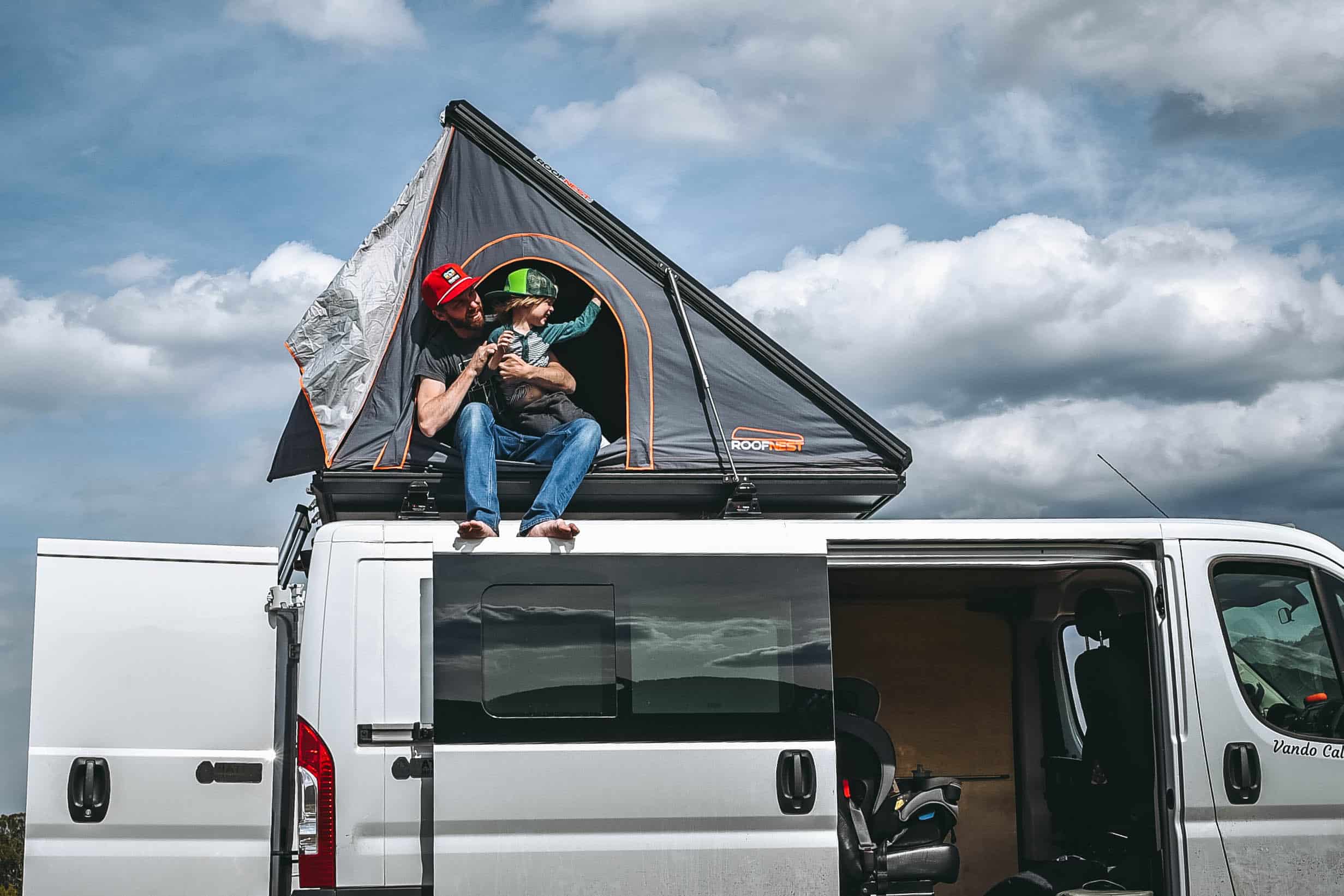 Man and kid sitting on a roof top tent on a campervan